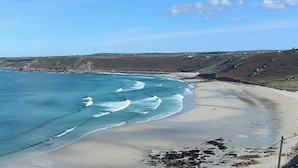 A coastal beach with clear blue water, sandy shore, and rocky cliffs in the background. - Ocean edge, beach side holiday cottage in Sennen Cove with 180’ panoramic Views (Sennen Cove)