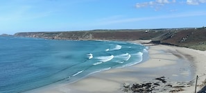 Ein Küstenstrand mit klarem, blauem Wasser, sandigem Ufer und felsigen Klippen im Hintergrund.