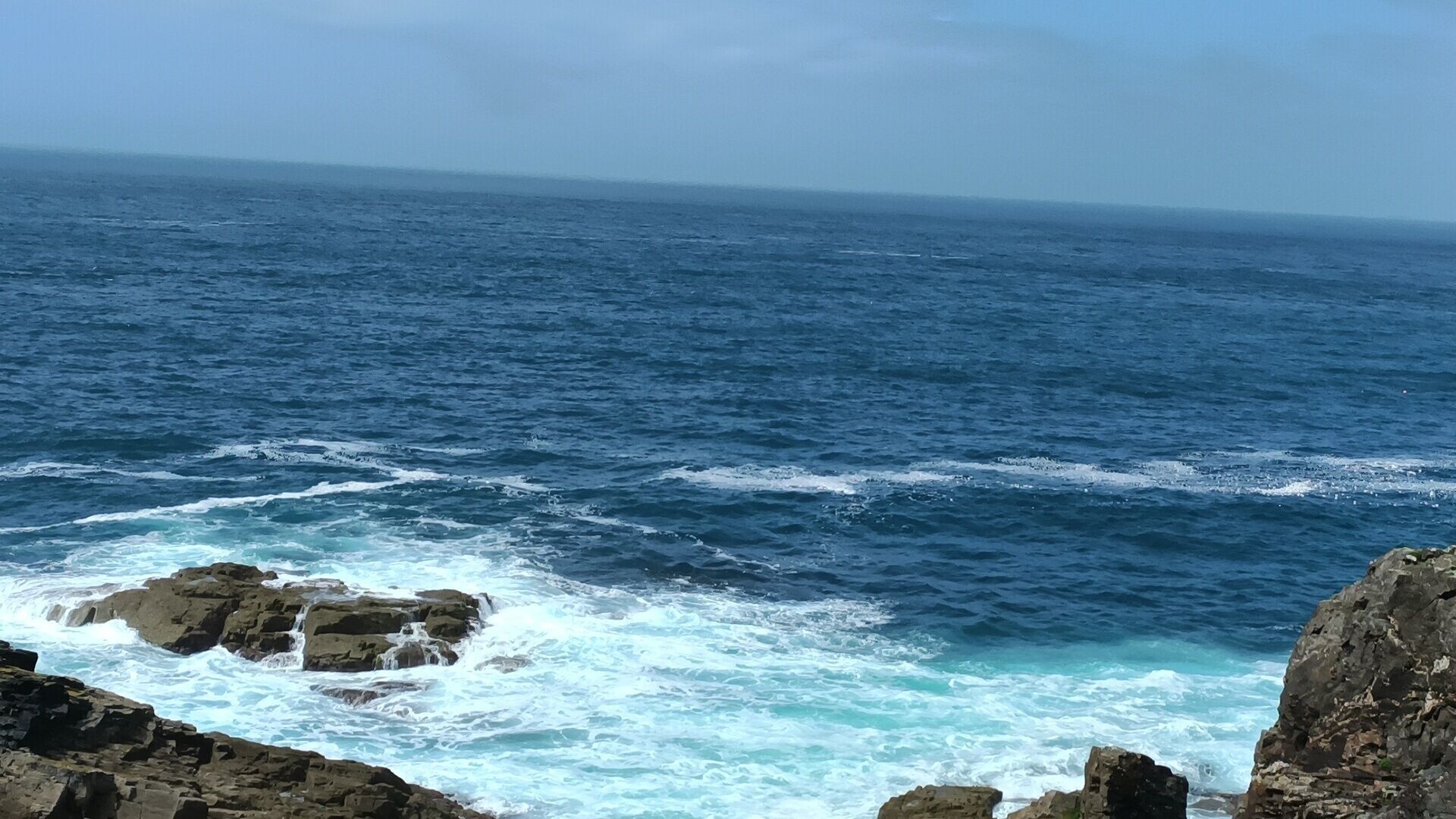 Uma paisagem costeira com ondas quebrando contra rochedos.