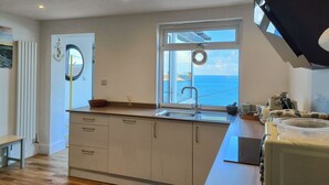 A modern kitchen with a view of the sea, a built-in oven, and a sink. - Ocean edge, beach side holiday cottage in Sennen Cove with 180’ panoramic Views (Sennen Cove)