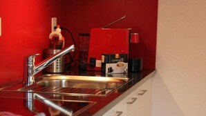 A modern kitchen with a red backsplash, stainless steel sink, and a coffee machine. - Ski-in/ Ski-out Nordostwand 4-Bett-Ferienwohnung by Interhome (Grindelwald)