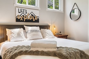 Una cama bien hecha con un cartel decorativo encima, una lámpara de noche y un espejo en la pared.