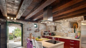 A rustic kitchen with a stone wall, wooden beams, a central island, and a view through an open archway. - in Makarska mit privatem Pool und außergewöhnlic by Interhome (Makarska)