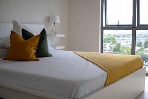 Ein Bett mit weißer Bettwäsche, einer gelben Decke und drei Kissen in verschiedenen Farben.