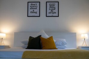 Une chambre d’hôtel avec un lit, deux citations encadrées au mur et des lampes de chevet.
