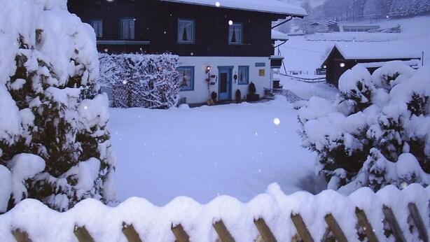 Ein mit Schnee bedecktes Haus mit einer sichtbaren Haustür, Fenstern und einem Schornstein.