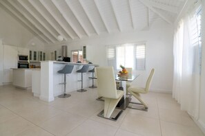 A spacious kitchen with white cabinetry, a central island, and bar stools. - Eshae Living - Uniquely Modern Beach House 3 (Priory)