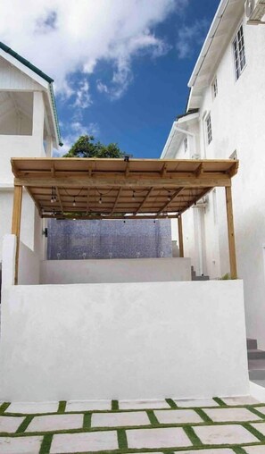 Un espace extérieur abrité, doté d’une structure en bois, d’un mur blanc et d’un mur recouvert de carreaux en arrière-plan.