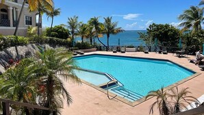 Ein Pool mit Meerblick, umgeben von Palmen und Liegestühlen.