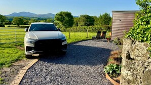 A white car parked on a gravel driveway, a stone wall, and a building with a sloped roof. - Hot Tub Getaway, Snowdon Views, Peaceful Stay (Llanfairpwllgwyngyll)
