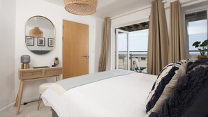Ein Schlafzimmer mit einem Bett, einem Nachttisch, einem Spiegel und Blick ins Freie.