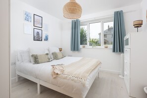 Ein Schlafzimmer mit einem weißen Bett, einem Nachttisch, einem Fenster mit Vorhängen und Wandbildern.