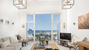 Ein Wohnzimmer mit Fernseher, Sofa und einem Balkon mit Meerblick.