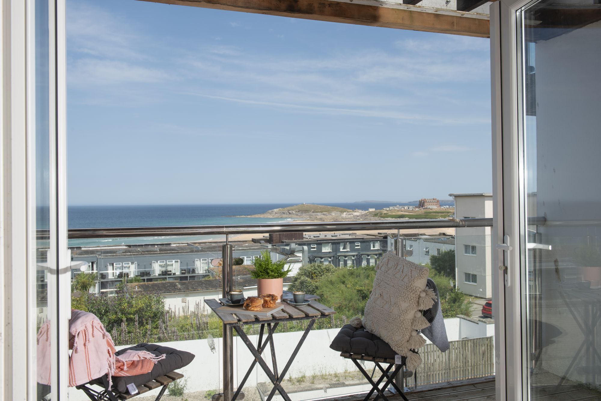 A balcony with a view of the sea, a table with a plant, and a chair.