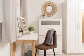 Ein Zimmer mit Schminktisch, Spiegel, Beleuchtung, einer Topfpflanze und einem Sessel.