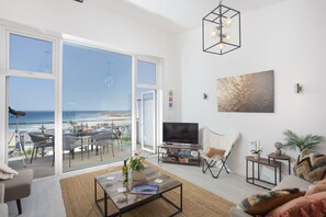 A spacious living room with a large sliding glass door leading to a balcony overlooking the beach. - Trelantis, 5 Gwelva - Sea view, 250m to beach, Pets welcome (Newquay)
