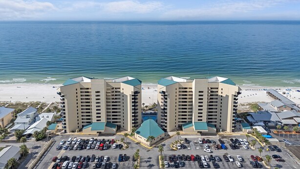 A beachfront hotel with a parking lot, multiple floors, and a view of the ocean. - Sunbird 612 East - Free Beach Chairs! (Panama City)