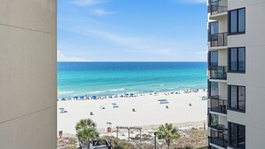 A beach view from a balcony with a clear sky, a sandy beach, and a building with balconies. - Sunbird 612 East - Free Beach Chairs! (Panama City)