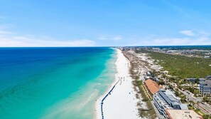 A coastal hotel with a beach view, a long sandy beach, and a cityscape in the background. - Crystal Beach Destin Home | 6BR w/ Private Pool & Carriage House | Walk to Beach (Destin)