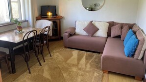 Uma sala de estar com sofá, televisão, mesa de jantar com cadeiras, tapete e janela com cortinas.