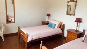 Quarto com cama de madeira, duas mesas de cabeceira com luminárias, um espelho e uma cadeira.
