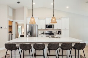 Uma cozinha moderna com armários brancos, eletrodomésticos de aço inoxidável e uma ilha grande com banquetas.