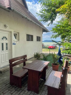 A building with a white exterior, a door, and windows. There is a table and bench outside. - Studio directly on the beach with air conditioning (Fonyód)