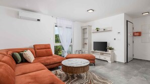 Uma sala de estar moderna com um sofá seccional, uma mesa de centro redonda, uma TV de tela plana e um armário embutido.