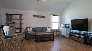 A living room with a sofa, armchair, coffee table, TV, and wooden flooring. - Peaceful 3-bedroom house in charming Stillwater for your getaway (Stillwater)