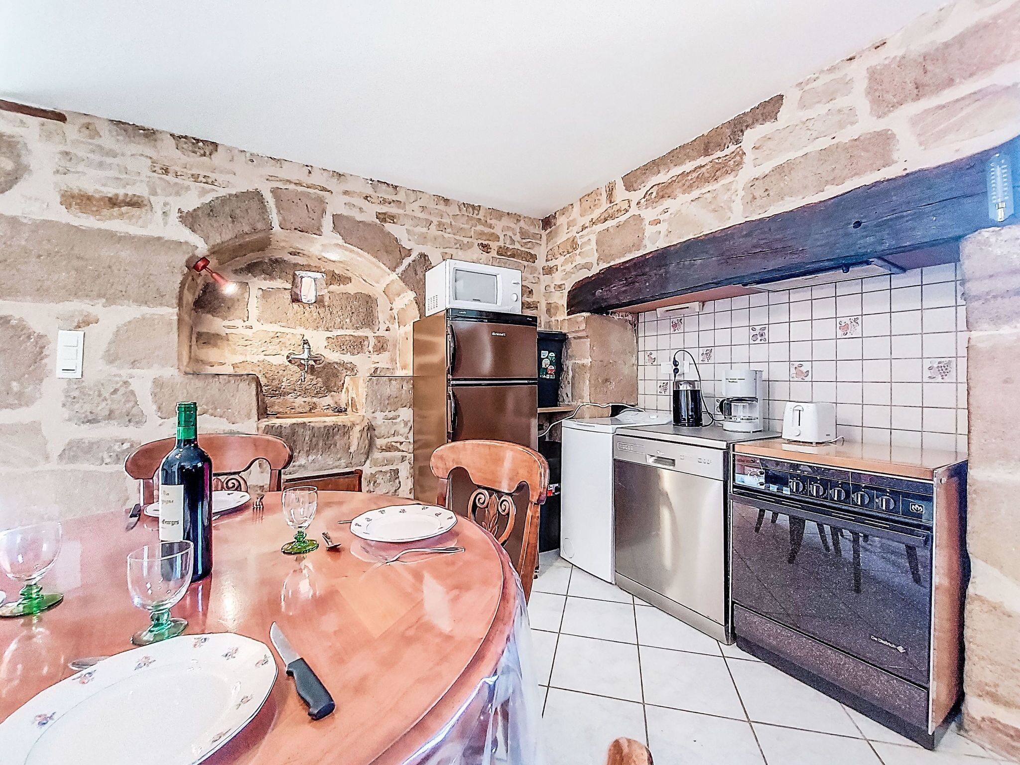 A kitchen with stone walls, a wooden dining table, and modern appliances.