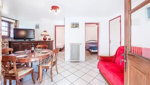 Un salon comprenant une table à manger, des chaises, un canapé rouge, un téléviseur et un radiateur.