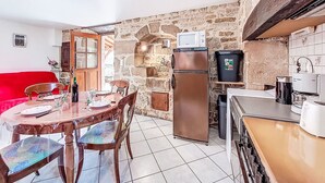 Une cuisine compacte avec un mur en pierre, un réfrigérateur, un four à micro-ondes et un coin repas comprenant des chaises et une table.