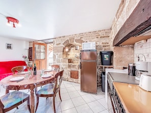 Une cuisine compacte avec un mur en pierre, un réfrigérateur, un four à micro-ondes et un coin repas comprenant des chaises et une table.
