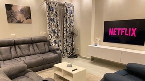 A living room with a grey sofa, a blue armchair, a white coffee table, and a TV displaying 'NETFLIX'.