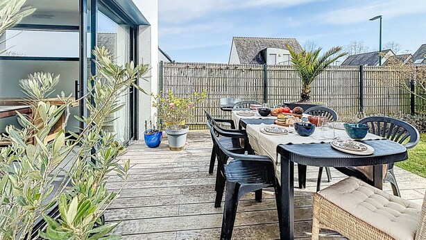 En udendørs terrasse med et spisebord, omgivet af stole og krukker med planter.