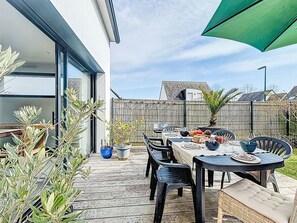 Eine Terrasse im Freien mit einem Esstisch, umgeben von Stühlen und Blumentöpfen.