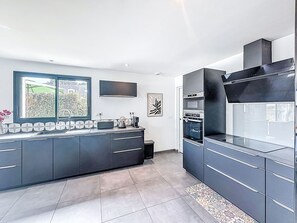 A modern kitchen with a large island, built-in oven, and a window overlooking a garden. - Maison Des Lupins by Interhome (Brec'h)