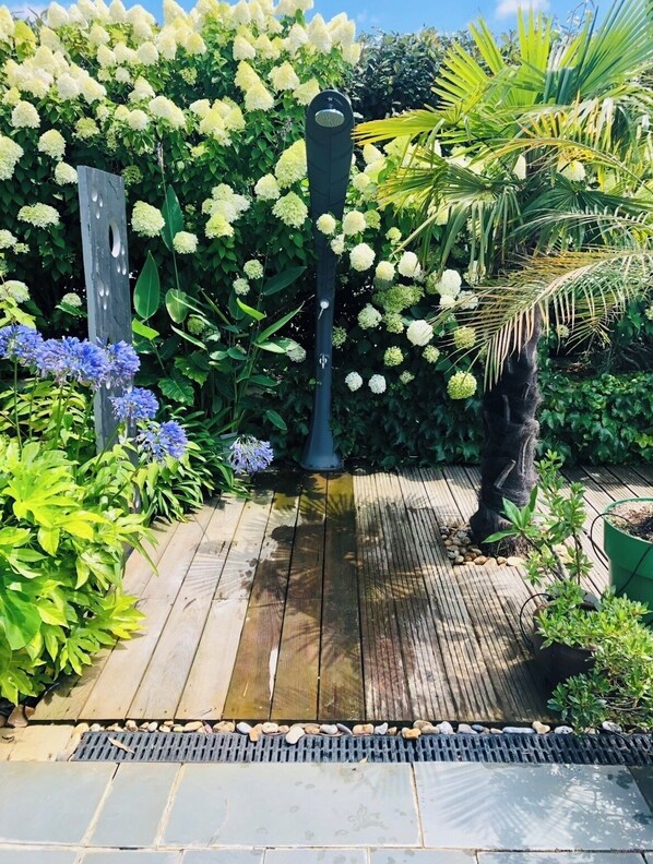 A wooden deck with a metal structure, surrounded by lush greenery and flowering plants.