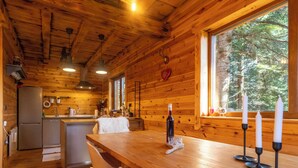 Interior de uma cabana de madeira com cozinha, área de jantar e grandes janelas.
