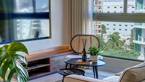 Ett modernt hotellrum med ett stort fönster, en platt-TV, en soffa, ett litet runt bord och ett bricka med teuppsättning.