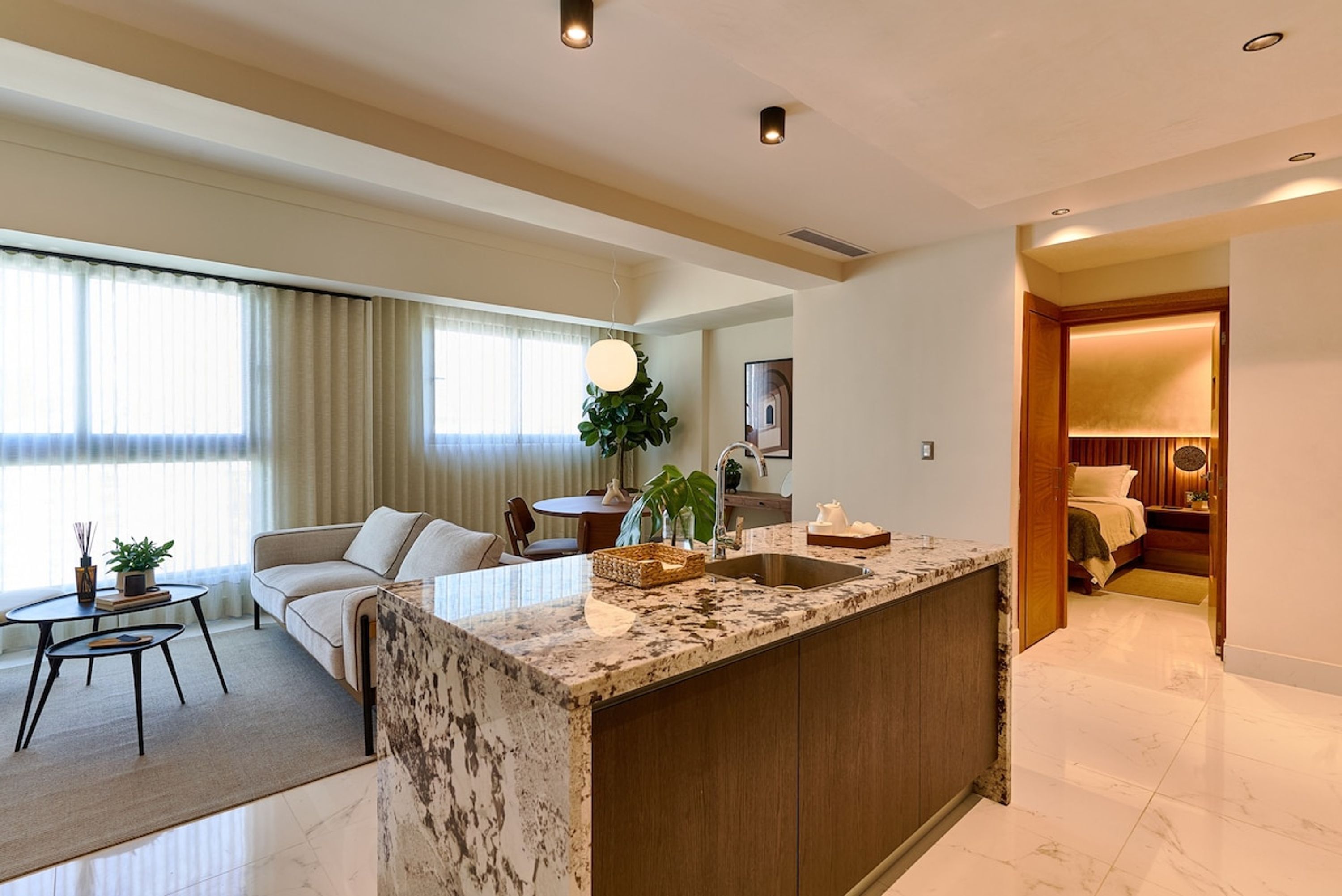 Una habitación de hotel moderna con una isla de mármol, un sofá, un comedor y vistas de la ciudad.