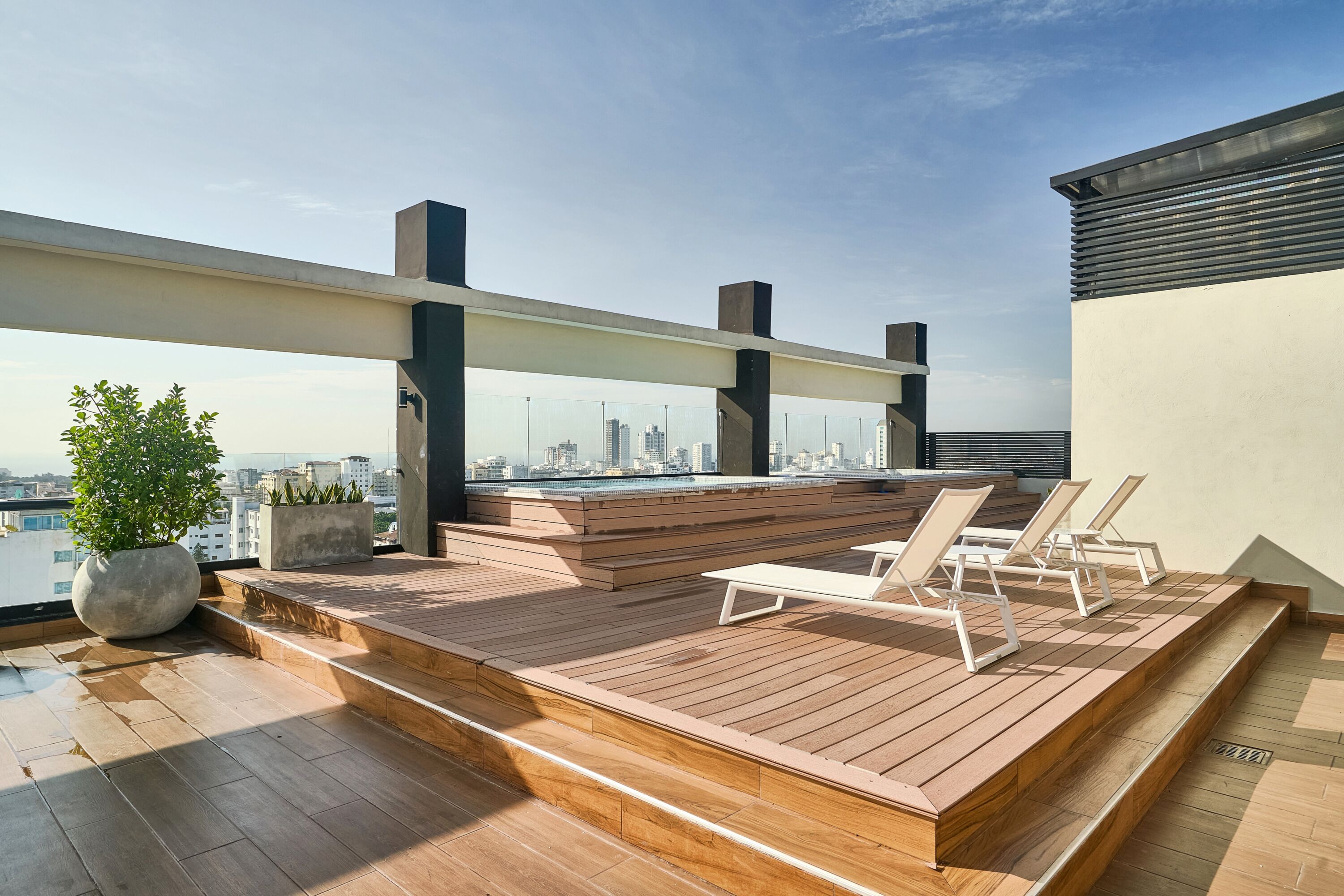 A rooftop terrace with wooden flooring, seating areas, and a city view.