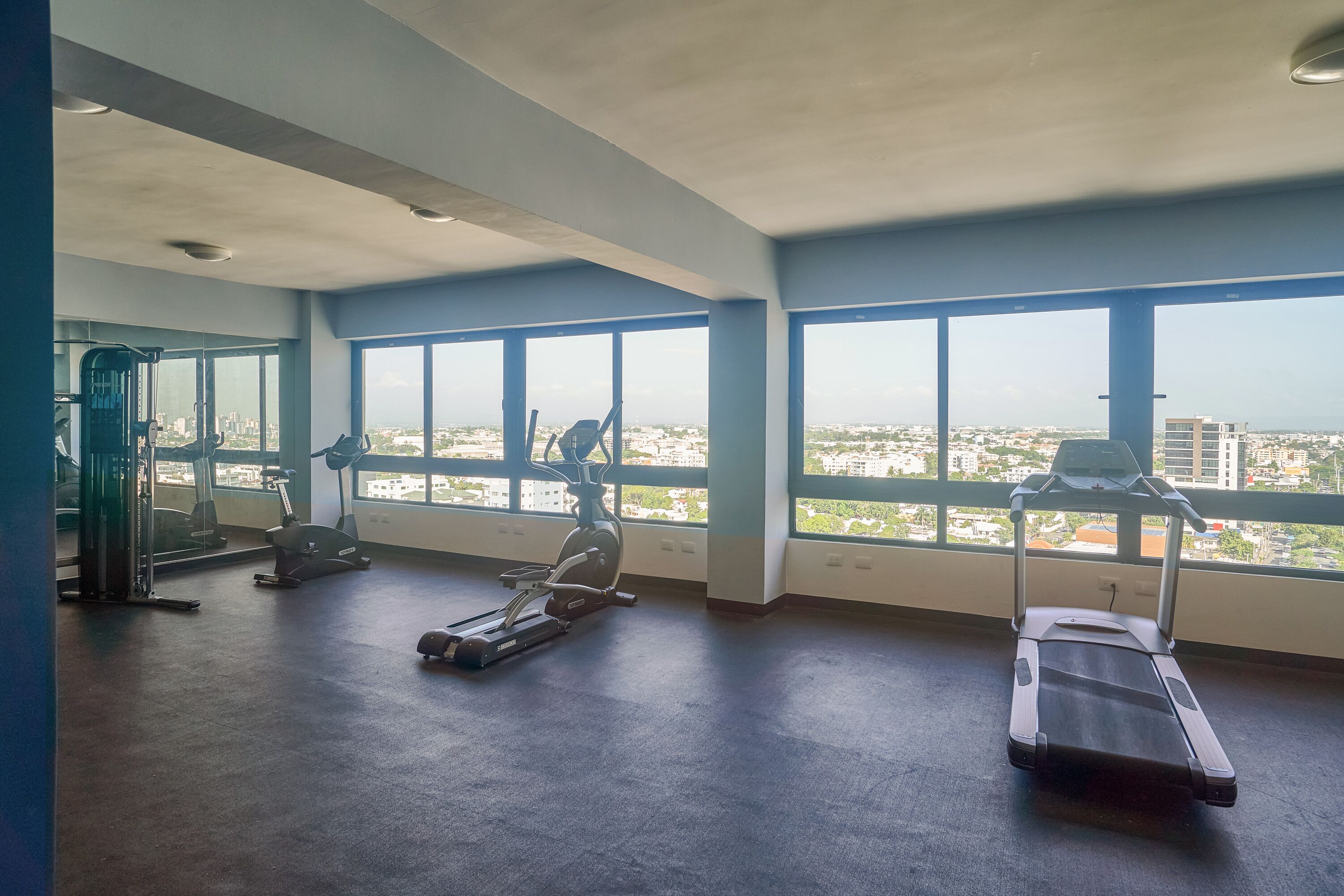 A gym with exercise equipment and large windows offering a city view.