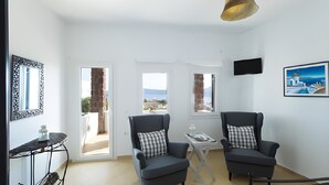 Une pièce comprenant deux fauteuils, une petite table, un téléviseur et de grandes fenêtres donnant sur un beau paysage.