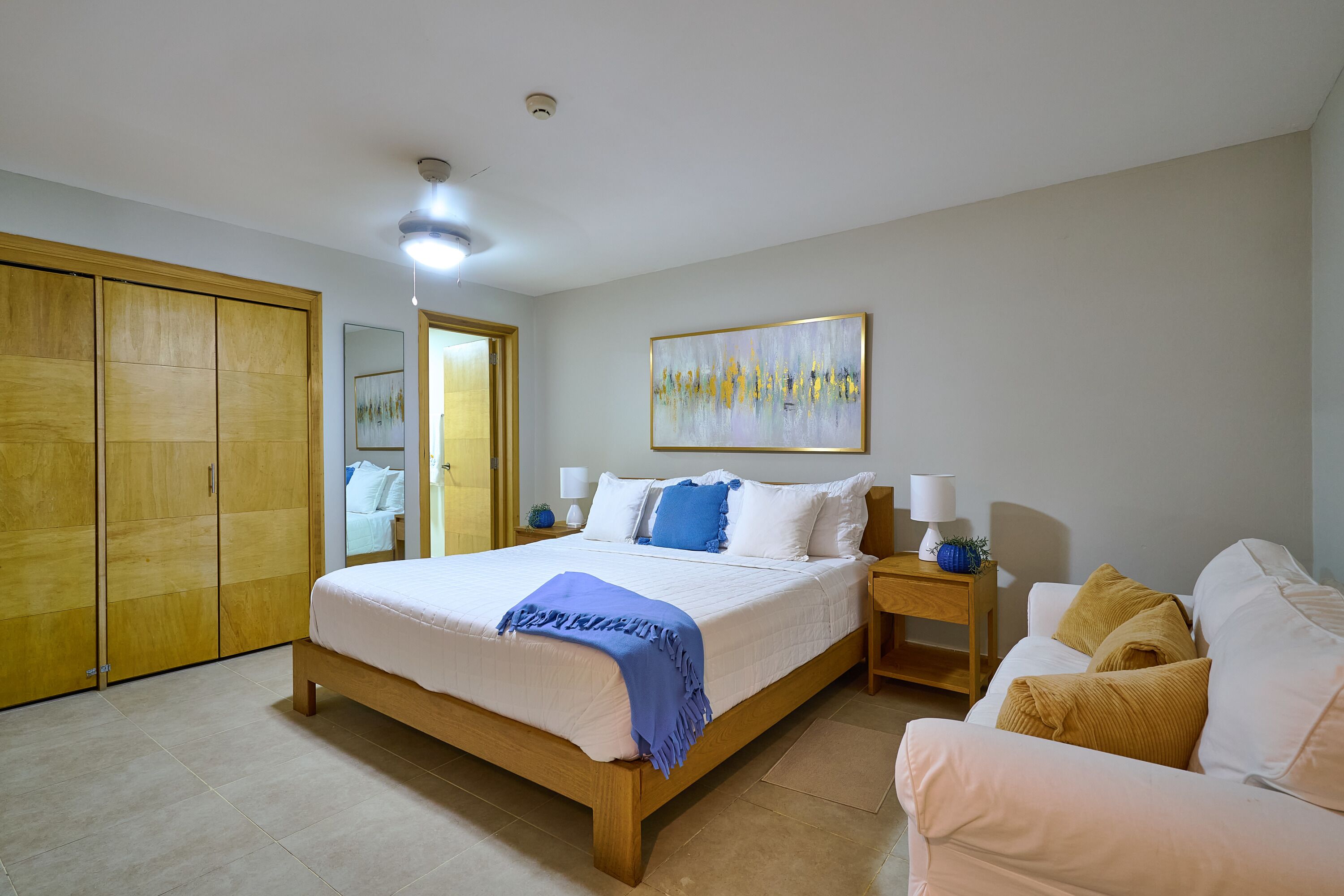 A bedroom with a bed, bedside tables, a wardrobe, a painting, and a sofa.