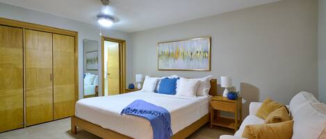 A bedroom with a bed, bedside tables, a wardrobe, a painting, and a sofa.