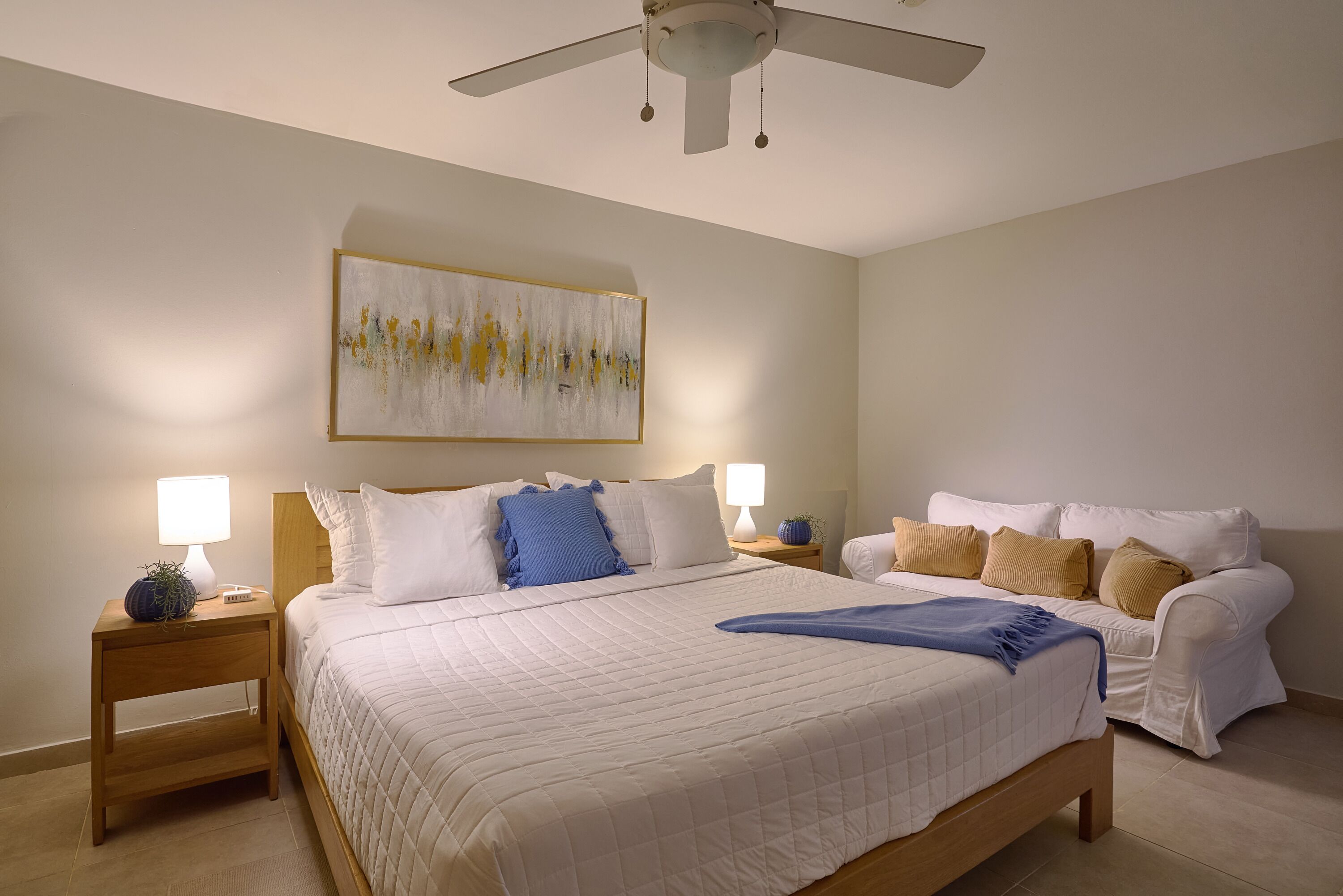 Une chambre à coucher avec un lit, des tables de chevet, un ventilateur de plafond et un tableau au mur.