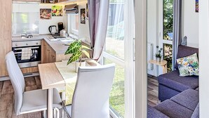 A compact kitchen with modern appliances, a dining area with a table and chairs, and a sofa in a living area with a view of greenery. - Tiny Haus Sigl by Interhome (Beilngries)