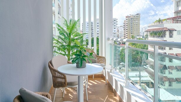 A balcony with wicker chairs, a small table, and a hanging light fixture. - The LUX Natural Art Downtownsd Pool Gym 2BR (Santo Domingo)