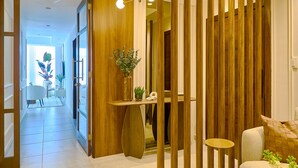 A modern interior with a wooden partition, a white sofa, a small round table, and a vase with flowers. - The LUX Natural Art Downtownsd Pool Gym 2BR (Santo Domingo)